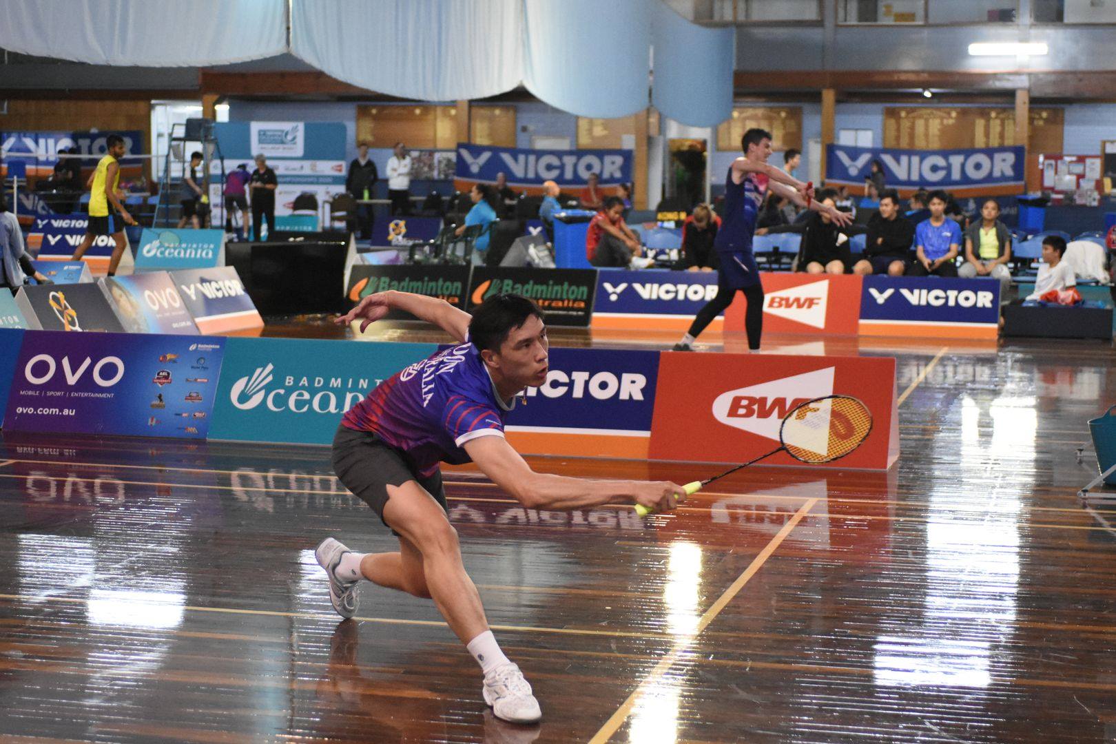 A badminton player lunging to reach the shuttle during an indoor competition