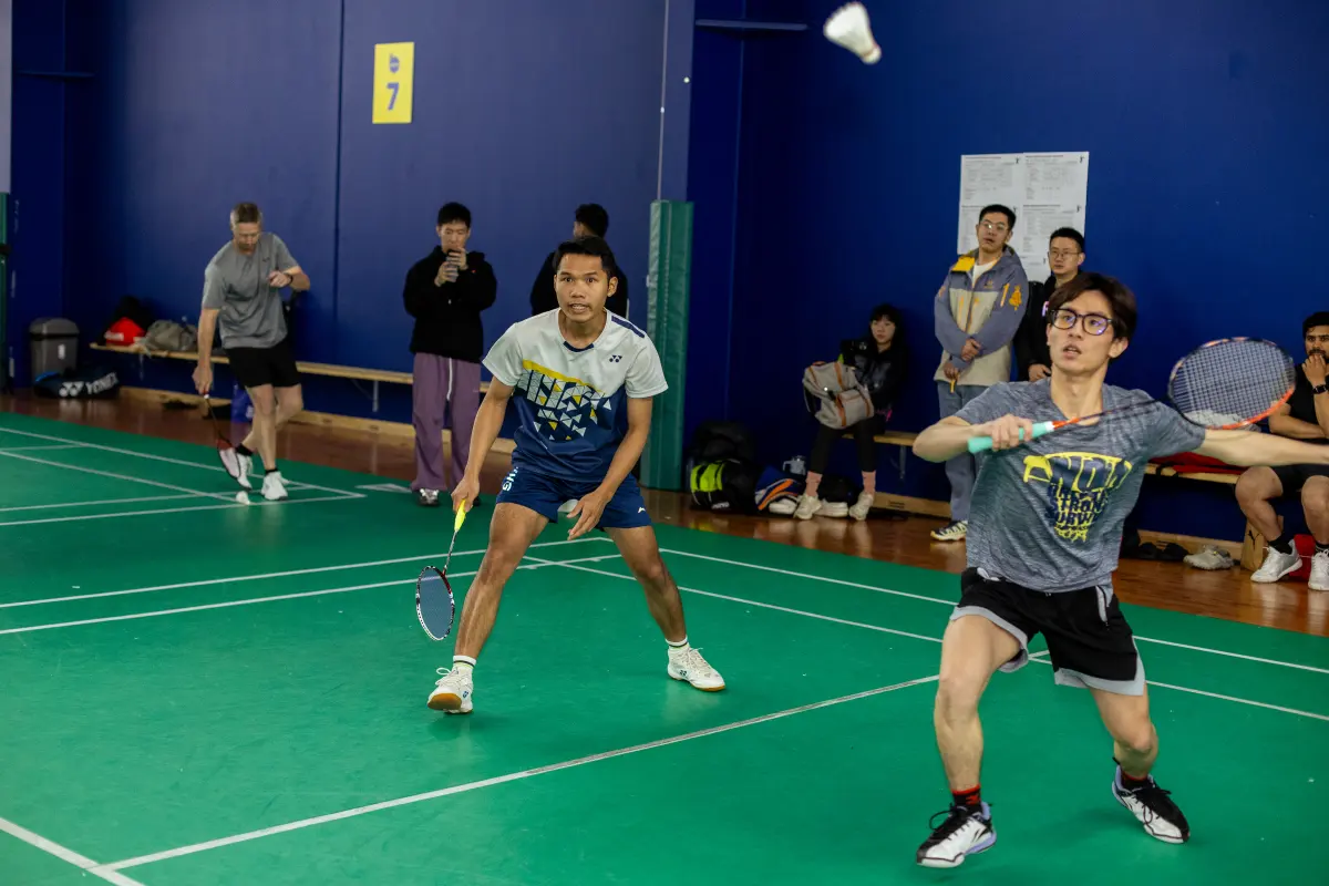 Badminton players watching the shuttle during an indoor doubles rally